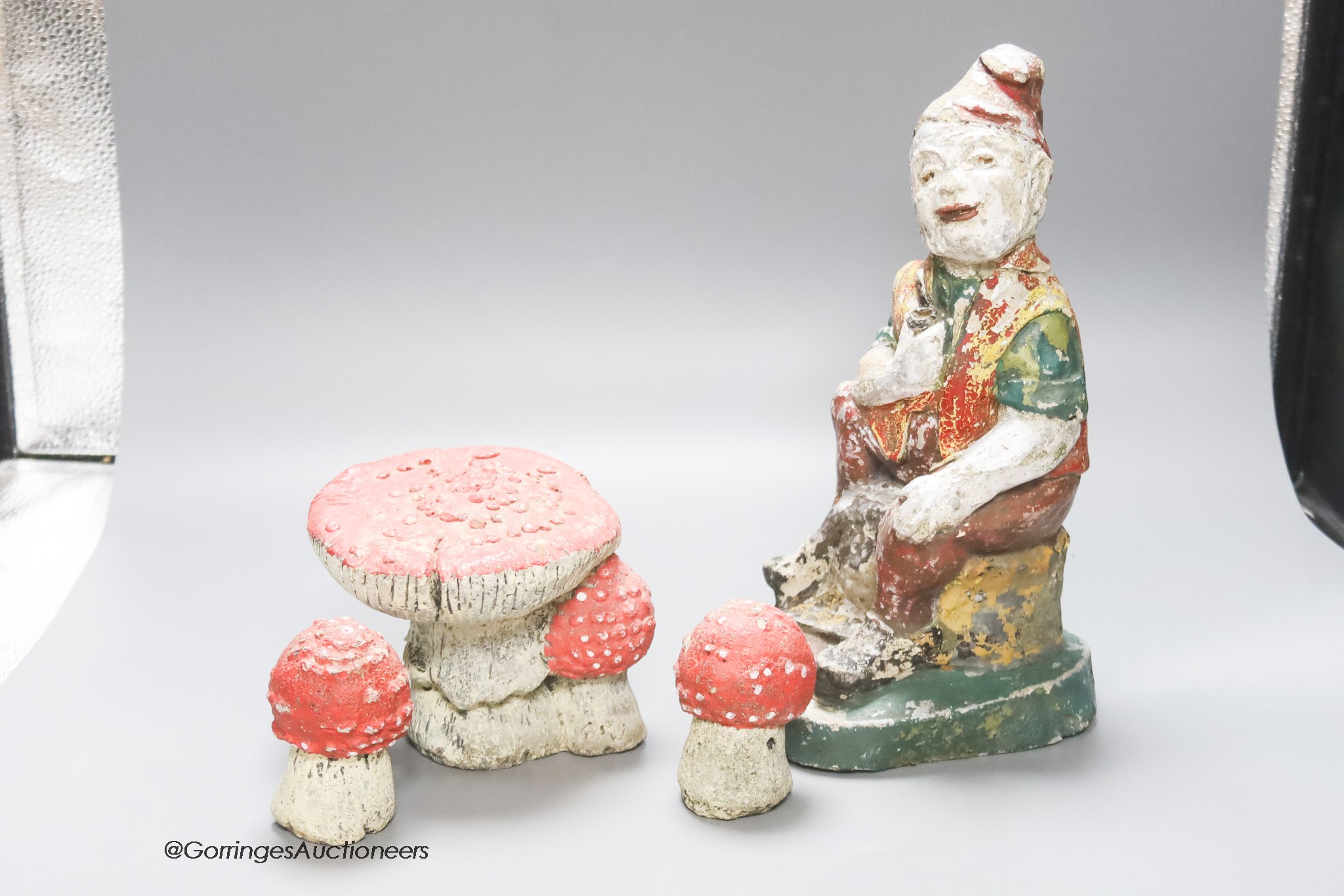 A composition seated garden gnome, height 29cm, and three toadstools (4)